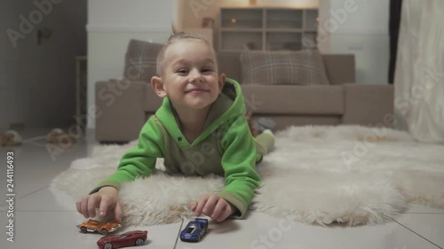 Portrait of little boy with stylish haircut playing with toycars lying on the floor on fluffy carpet. photo