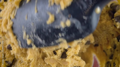 Macro shot of mixing raw chocolate chip cookie dough in 4k. A black, silicone spatula stirs incorporates bittersweet chocolate morsels. Extreme closeup for step by step recipes and homestyle baking.