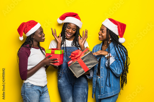 Beautiful three african women holding christmas presents isolated on yellow background