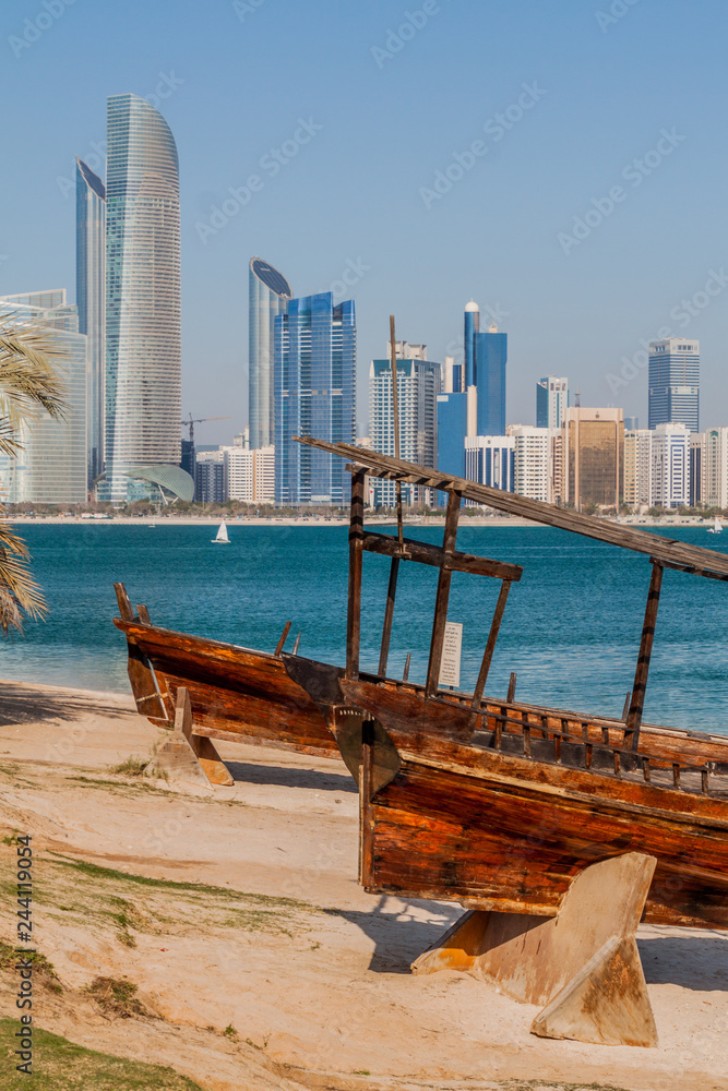View of the skyline of Abu Dhabi from the Marina Breakwater beach with wooden boats, United Arab Emirates