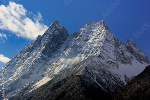 Siguniangshan - Four Girls Mountain National Park in Sichuan Province, China. ShuangQiao Valley Scenic Area, Snow Capped Jagged Mountains with clouds forming at the summit. Blue Sky, Snow Mountains photo