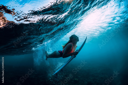 Attractive surfer woman dive underwater with under wave and sun light.