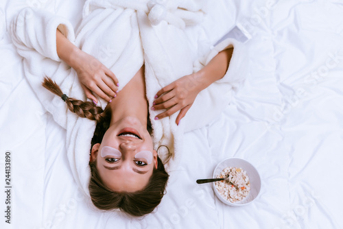 Foto happy young girl in a white terry robe lies on the bed, under the eyes of silico