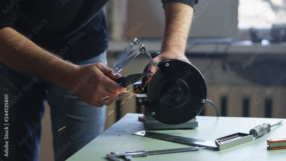 Master works for grinding machine. Man with glasses handles a part. Working process. Sparks fly. Close-ups