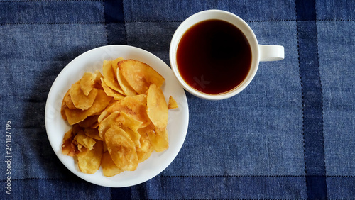 Sweet crispy banana chips on white served with hot tea dish on blue background and space for write wording, a way to preserve agriculture fruit and adding value to growth business export worldwide.