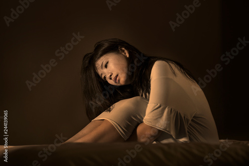 dramatic portrait of young beautiful and sad Asian Japanese woman crying desperate on bed awake at night suffering depression crisis and insomnia feeling broken heart pain
