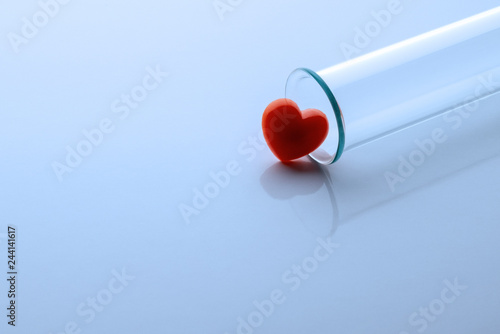 One red heart and a medical or laboratory glass test tube. Toned in blue. Close-up. Copy space.