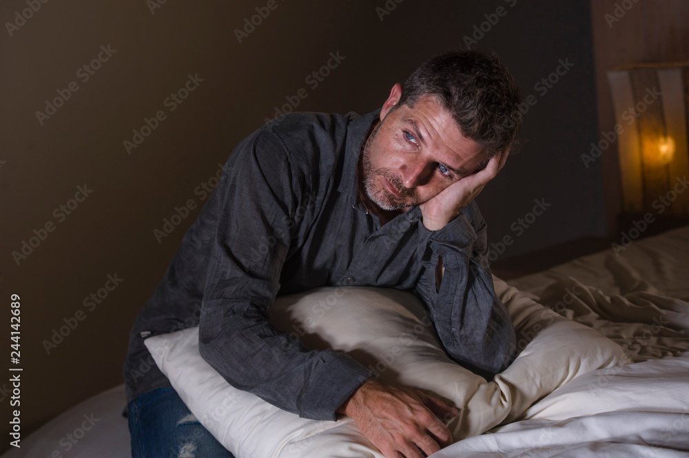 Obraz premium young attractive sad and depressed man on bed suffering anxiety crisis and depression problem feeling overwhelmed and stressed late at night on dramatic light