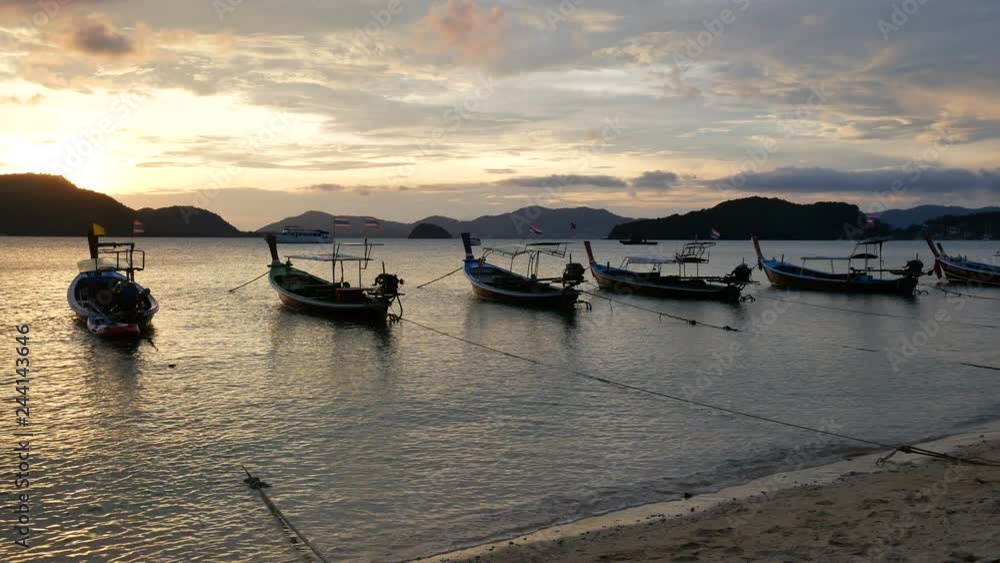 moving sea wave water at sandy beach and moving thai flag on long tail boat tie with rope in ocean, silhouette mountain, reflection in water with sun beam light at sunset time moving sea wave water at sandy beach and moving thai flag on long tail boat tie with rope in ocean, silhouette mountain, reflection in water with sun beam light at sunset time