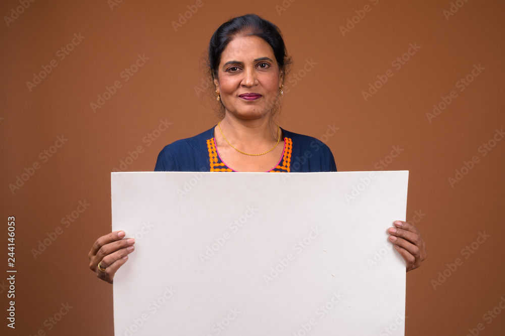 Mature beautiful Indian woman holding empty white board with copyspace Mature beautiful Indian woman holding empty white board with copyspace