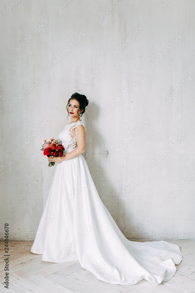 Beautiful girl in a wedding dress with a bouquet. Bride in a bright Sunny Studio.