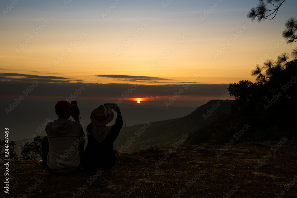Image of sunset or sunrise on orange and yellow horizon with a silhouette of a couple in natural surrounding