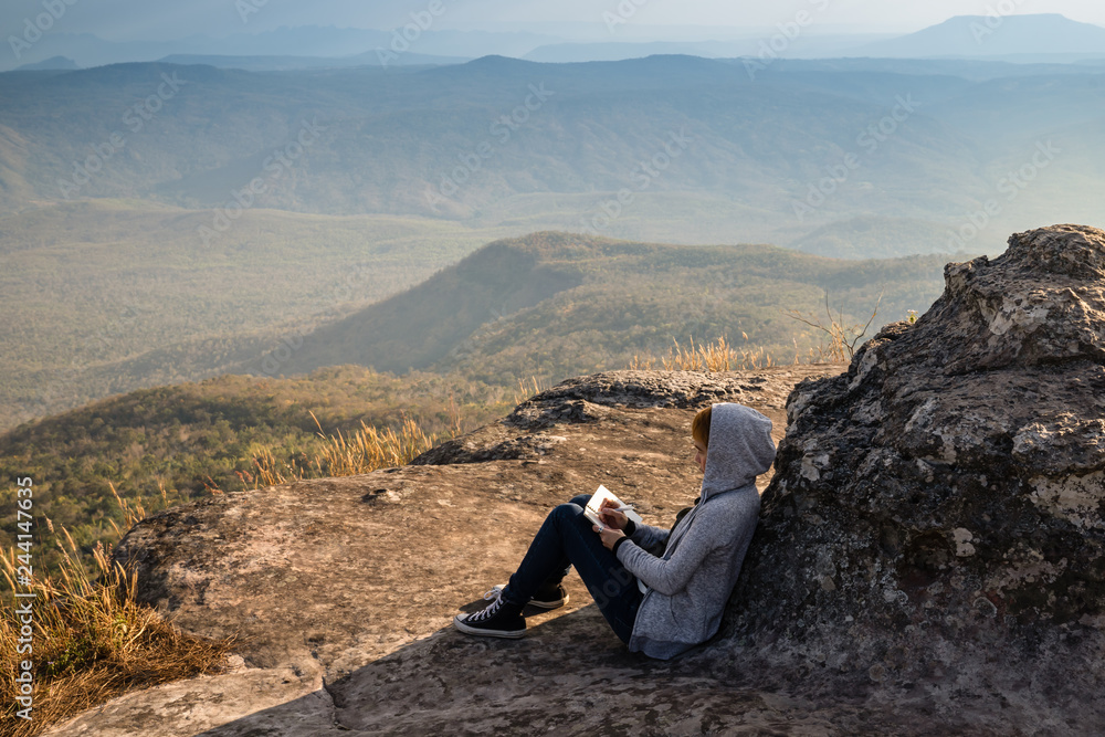 A woman sitting reading and writing looking out at beautiful natural view