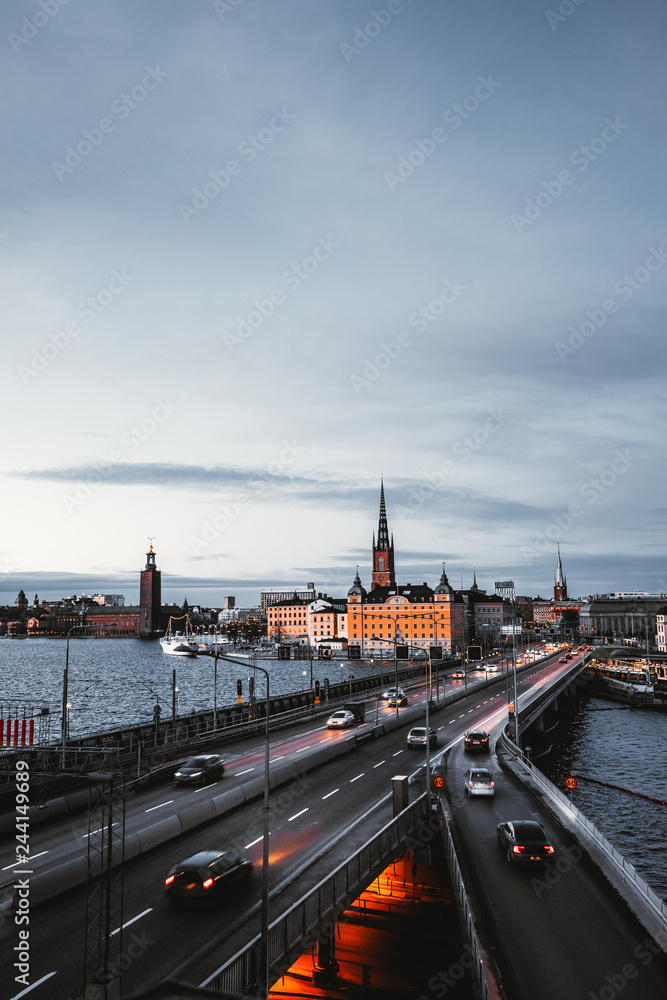 Evening cityscape view on Stockholm city center, church and city hall on the background and highway bridge in front, night lights, dark blue sky