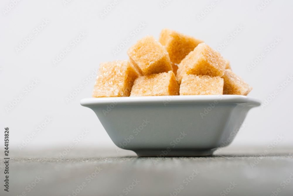 brown sugar cubes on white square dish, dark wood table brown sugar cubes on white square dish, dark wood table