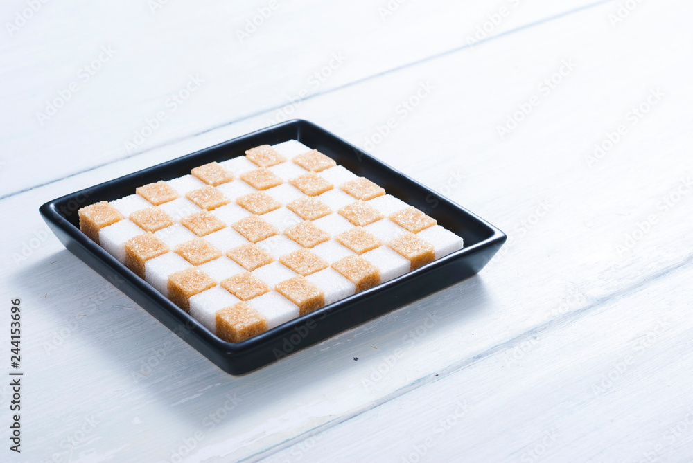 white and brown sugar nubs on black square plate, bright wood table background white and brown sugar nubs on black square plate, bright wood table background
