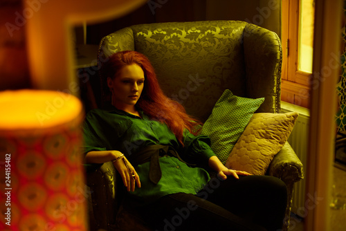 Mirror reflection of Ginger lady posing in loft apartment in Tbilis. She wears green shirt and black jeans. Flat has big window. Walls are of red bricks. Photo has vintage style and is yellowish. photo