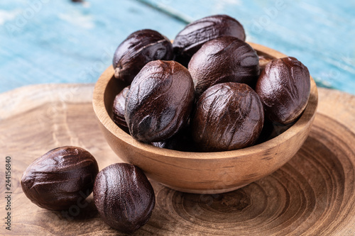 Whole inshell nutmeg nuts in a bowl on blue rustic wooden table.