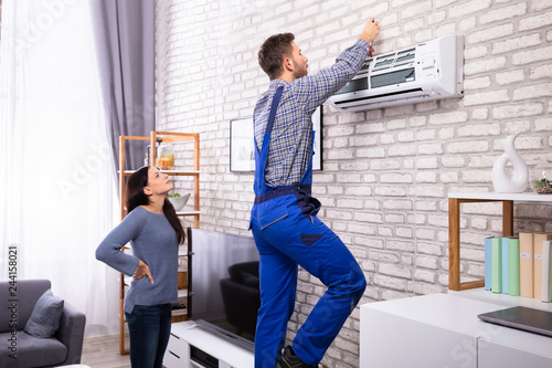 Woman Looking At Technician Repairing Air Conditioner