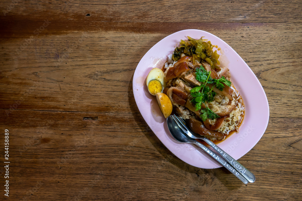 The pink plastic dish of pork stewes with rice , egg and parsley on the wooden table in restaurant. 