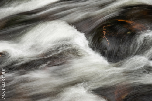 Detail intimate landscape image of river flowing over rocks with long exposure motion blur
