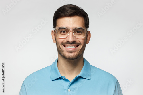 Smiling modern nice guy in blue polo shirt and trendy trasparent eyeglasses, isolated on gray background © Damir Khabirov