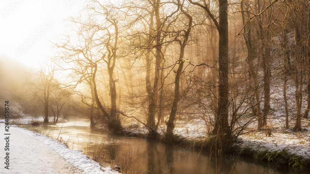 Stunning vibrant golden glow sunrise over landscape of stream in Winter forest with snow on gorund Stunning vibrant golden glow sunrise over landscape of stream in Winter forest with snow on gorund
