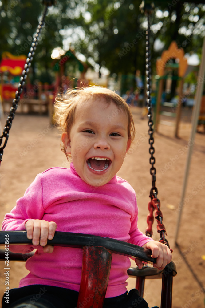 Little girl with funny facial expression swinging on the swings on the Playground Little girl with funny facial expression swinging on the swings on the Playground