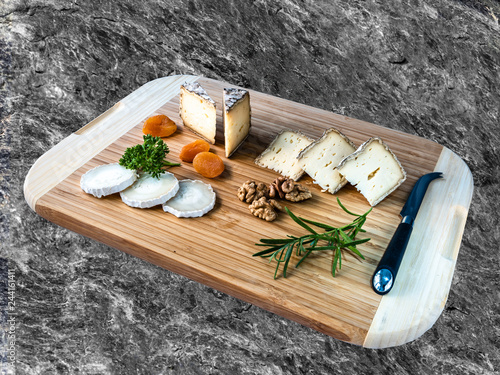 Cheese from France named Tommette des Alpes and white round goat cheese with dried apricot, rozmarin. nuts and parsley on wooden desk with shadow on natural stone's background photo