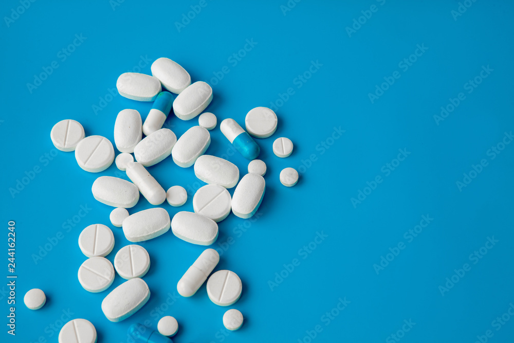 Scattered white pills on blue table. Mock up for special offers as advertising, web background or other ideas. Medical, pharmacy and healthcare concept. Copy space. Empty place for text or logo Scattered white pills on blue table. Mock up for special offers as advertising, web background or other ideas. Medical, pharmacy and healthcare concept. Copy space. Empty place for text or logo