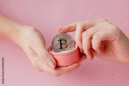 Woman's hands holding bitcoin in pink gift box on a pink background, symbol of virtual money