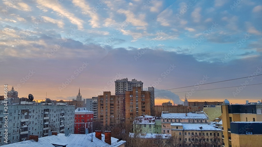 Fototapeta premium Świt w Moskwie nad domami i piękny wschód słońca miasta odbijający się w oknach wieżowców i wieżowców w mroźny zimowy poranek z jasnym niebem, chmurami i dymem z rur fabryk