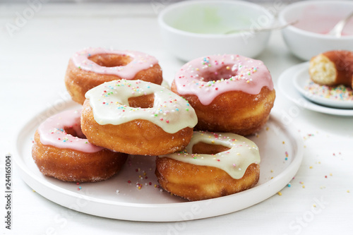 Homemade donuts decorated with colored icing and colored sugar on a light background.