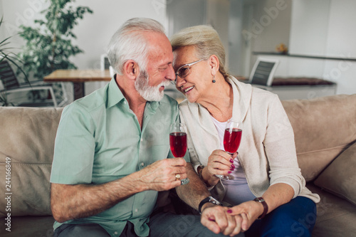 Cheerful senior couple moving into new home smiling at each other and drink wine.
