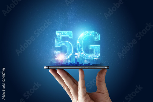 Creative background, male hand holding a phone with a 5G hologram on the background of the city. The concept of 5G network, high-speed mobile Internet, new generation networks. Copy space photo