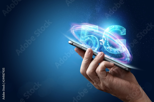 Creative background, male hand holding a phone with a 5G hologram on the background of the city. The concept of 5G network, high-speed mobile Internet, new generation networks. Copy space, photo