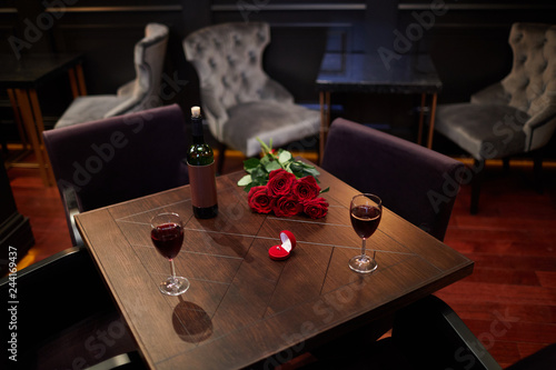 Фотография Wooden table with bottle of wine, two wineglasses, bunch of red roses and velvet