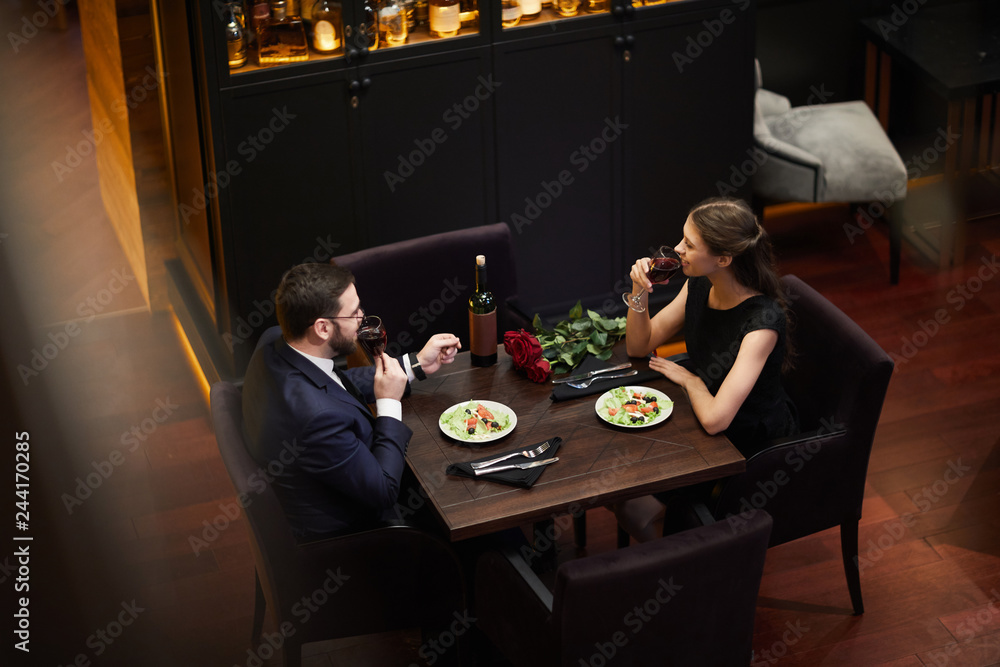 Fotografie Young amorous dates sitting by table in luxurious restaurant, drinking red wine