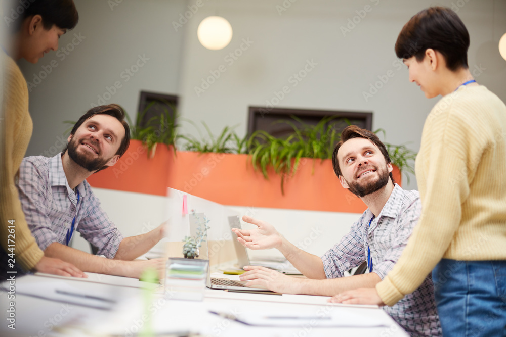 Confident broker or analyst showing his colleague online data while discussing it at working meeting in office Confident broker or analyst showing his colleague online data while discussing it at working meeting in office