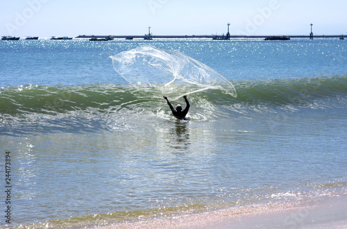 A fisherman in water throws his dragnet to the ocean  photo