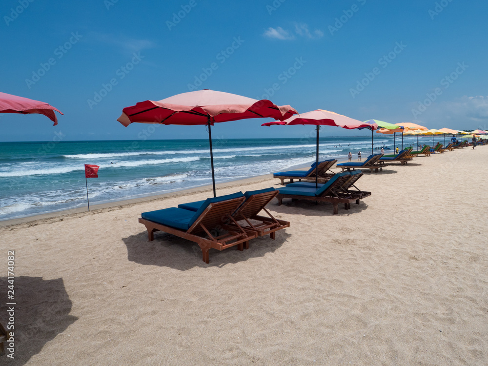 Colorful umbrellas stay on yellow sand beach with blue sea and blue sky on background. Concept for rest, relaxation, holidays, spa, resort. Kuta beach, Bali, Indonesia, October, 2018