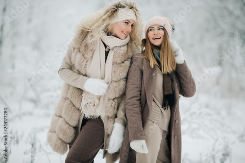 Portrait of two happy blonde women in hat on walk in winter forest
