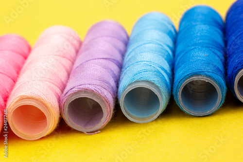 Group of colorful spools of thread used to sewing, needlework and embroidery over bright yellow background