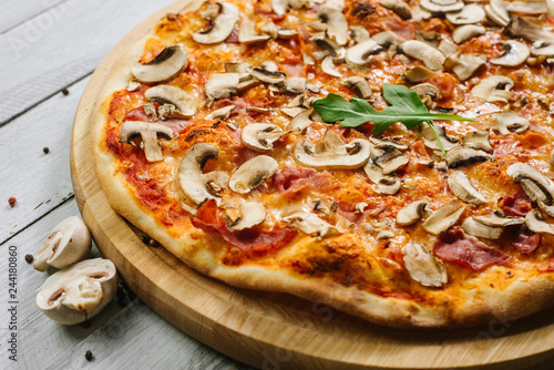 Tasty pizza Caprizzioza with tomato sauce, ham and champignons on the white wooden background