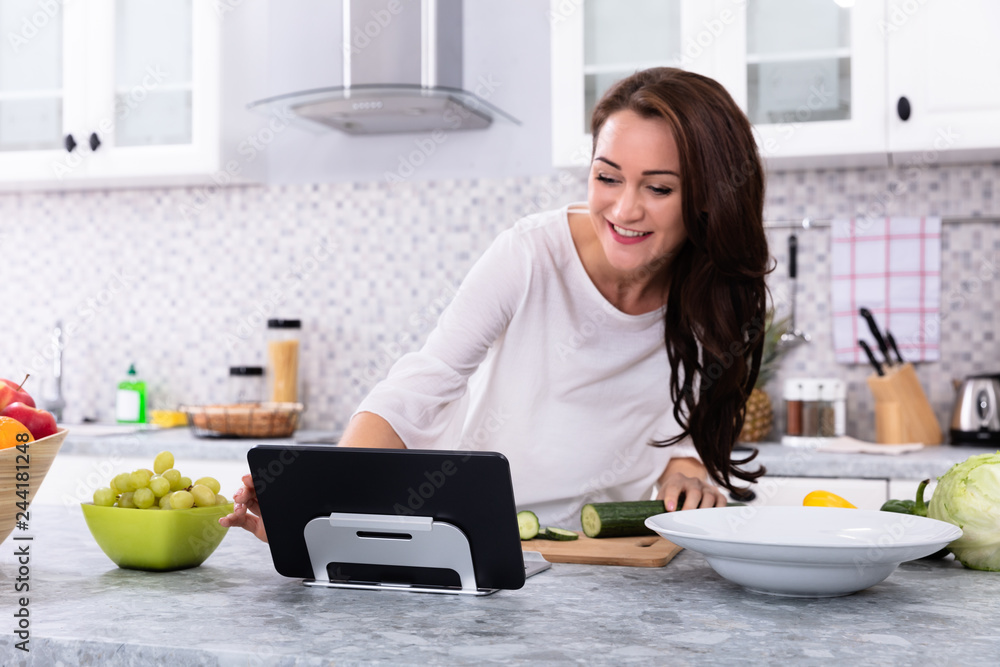 Woman Using Digital Tablet While Cooking Food Woman Using Digital Tablet While Cooking Food