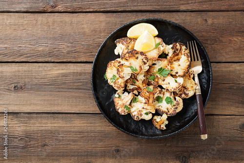 Black plate with tasty grilled cauliflower on wooden table.