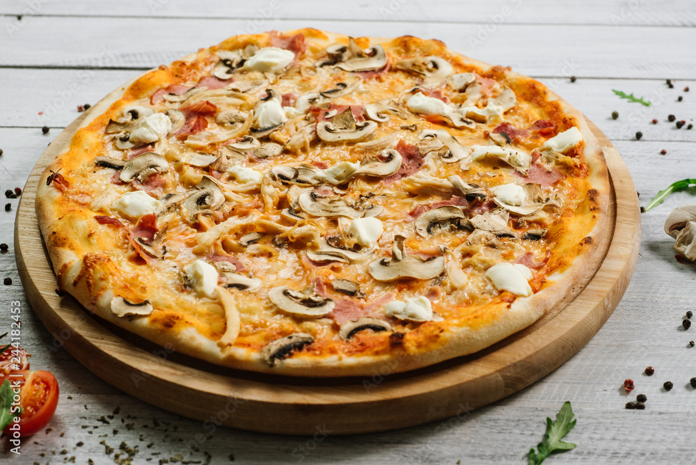 Tasty pizza with mozzarella, hum, chicken fillet, and champingnons on the white wooden background Tasty pizza with mozzarella, hum, chicken fillet, and champingnons on the white wooden background