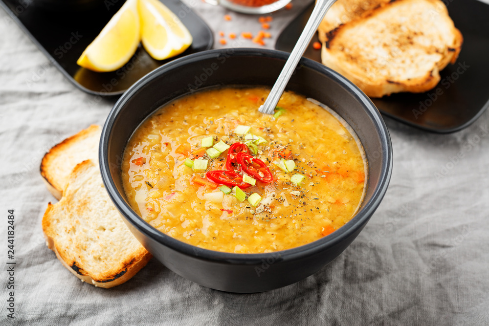 Lentil soup with bread in a dark ceramic bowl on a gray textile background . Lentil soup with bread in a dark ceramic bowl on a gray textile background .