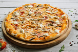Tasty pizza with mozzarella, hum, chicken fillet, and champingnons on the white wooden background