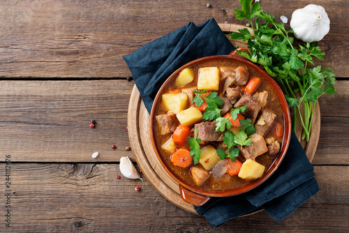Obraz na plátně Meat stewed with potatoes, carrots and spices in ceramic pot on wooden background